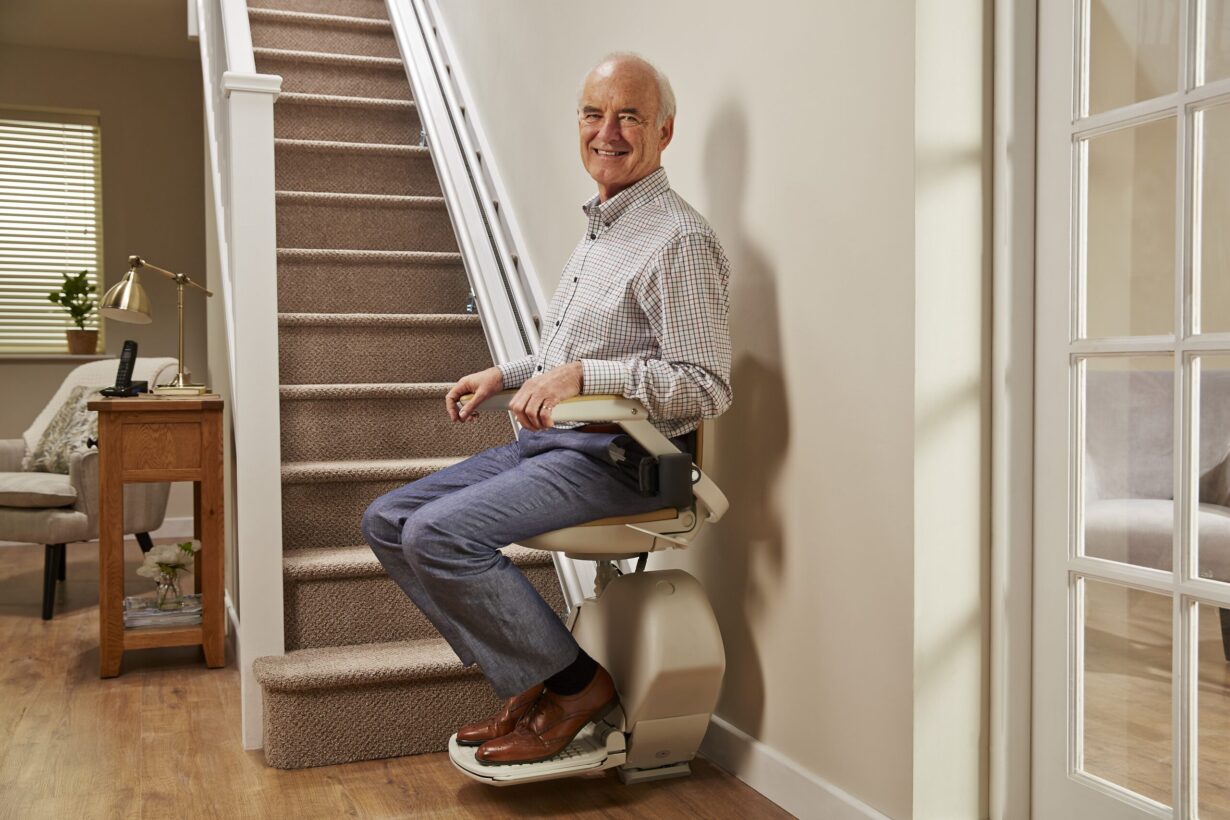 Smartly dressed older man sat in a stairlift at the foot of his stairs