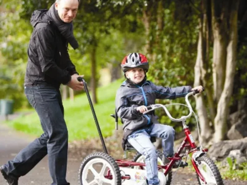 An older man pushing a young boy outside on a theraplay trike