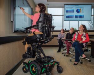 lady in a permobil powerchair in an elevated position teaching a class